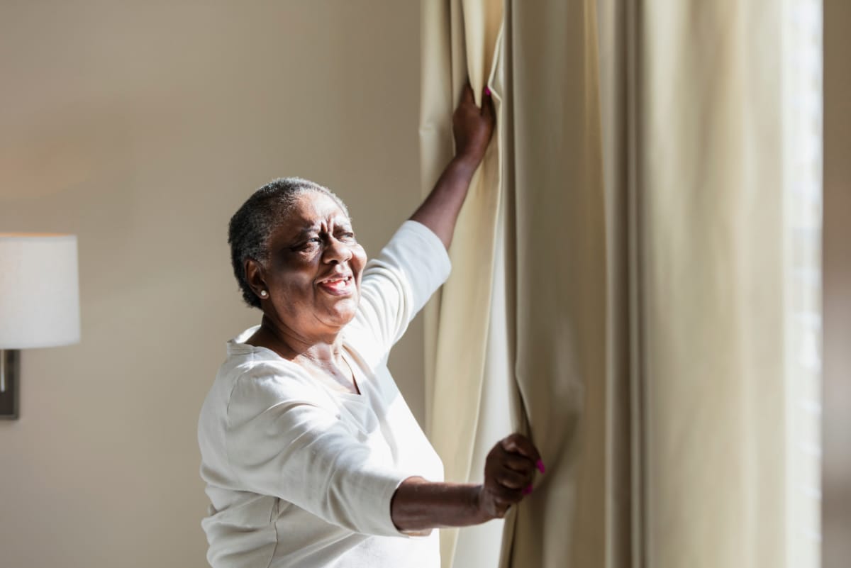 Senior woman opening curtains to let in morning light
